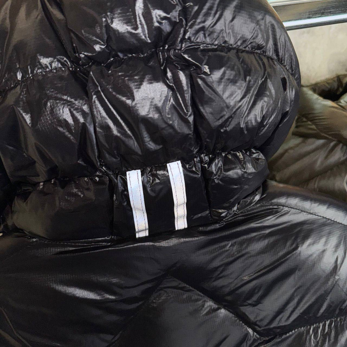Black bubble jacket with button front, gathered hood, and two white chest stripes