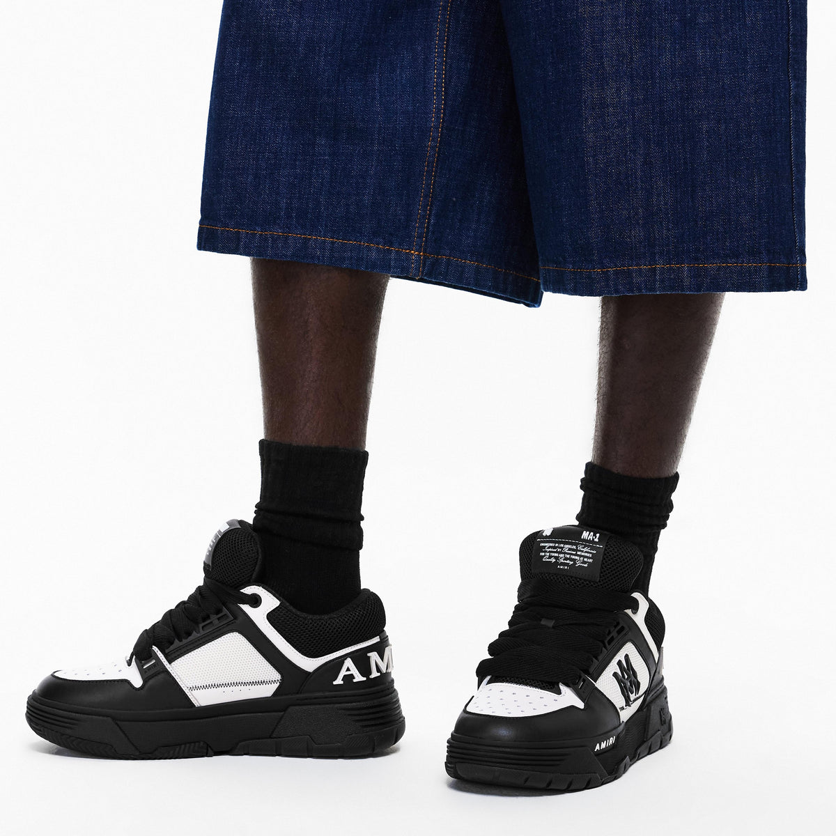 Chunky trainers worn with black socks and blue denim shorts; lace-up black/white