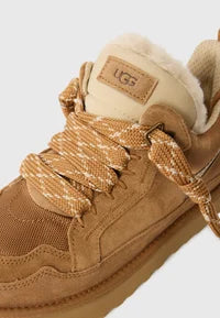 Nahaufnahme: chestnut-braunes Obermaterial, Schnürsenkel und UGG-Label am Schaft
