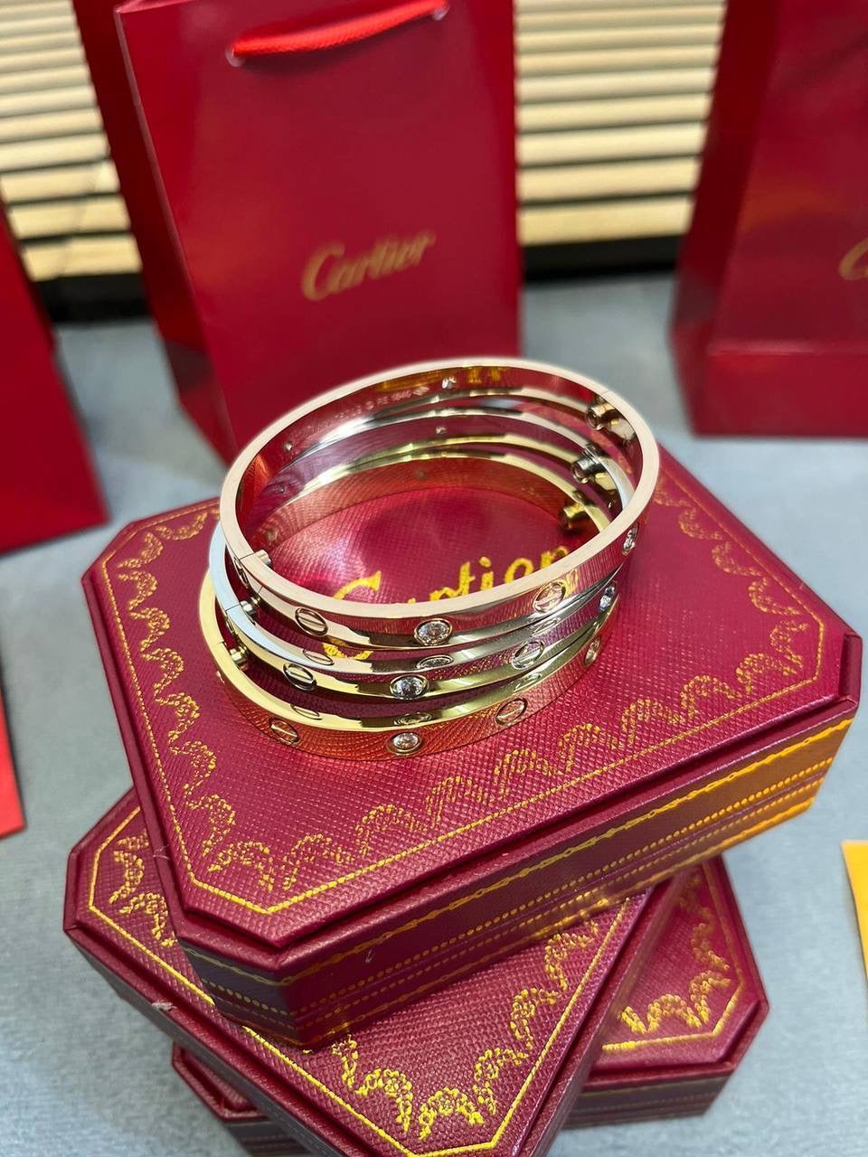 Gold and silver tone love bracelets stacked on maroon Cartier gift box