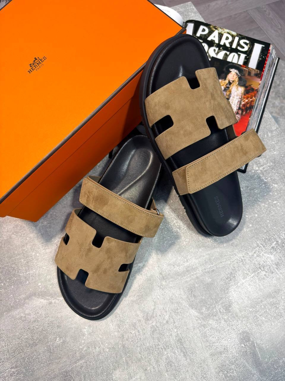 Tan suede slide sandals with black cutout band and wide strap, pair on display