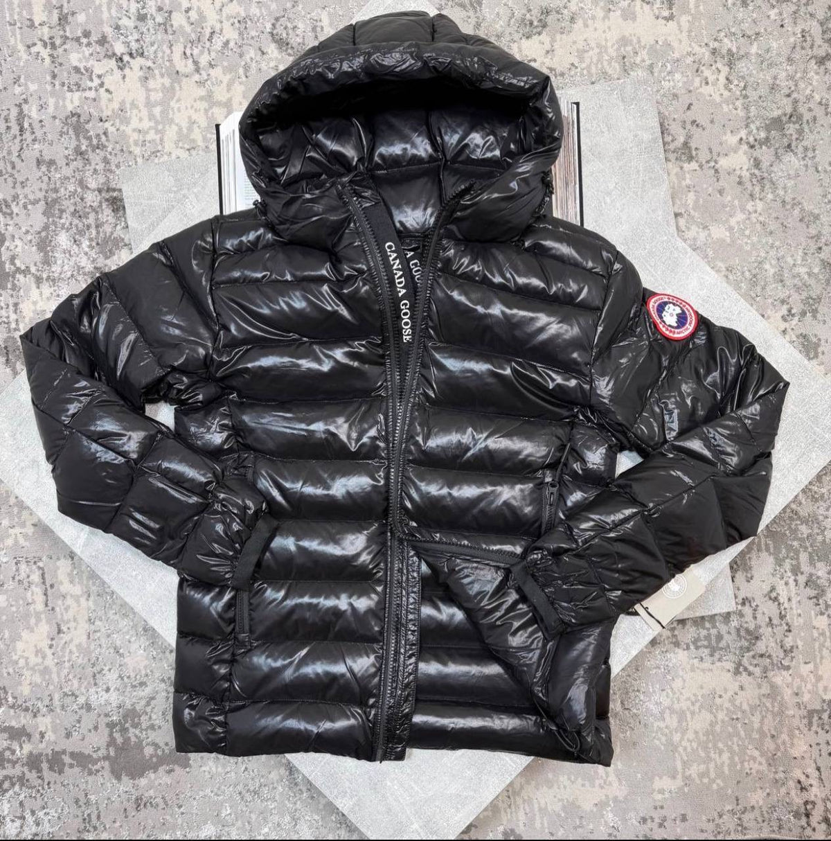 Black hooded puffer jacket with full-zip front and red-bordered round sleeve patch