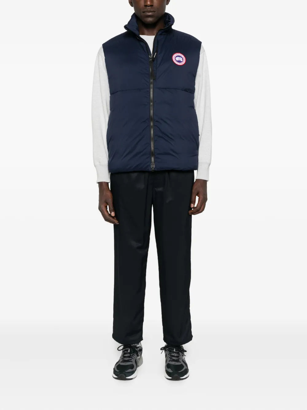 Navy puffer gilet with hood, zip front, circular logo patch; worn over white sleeves