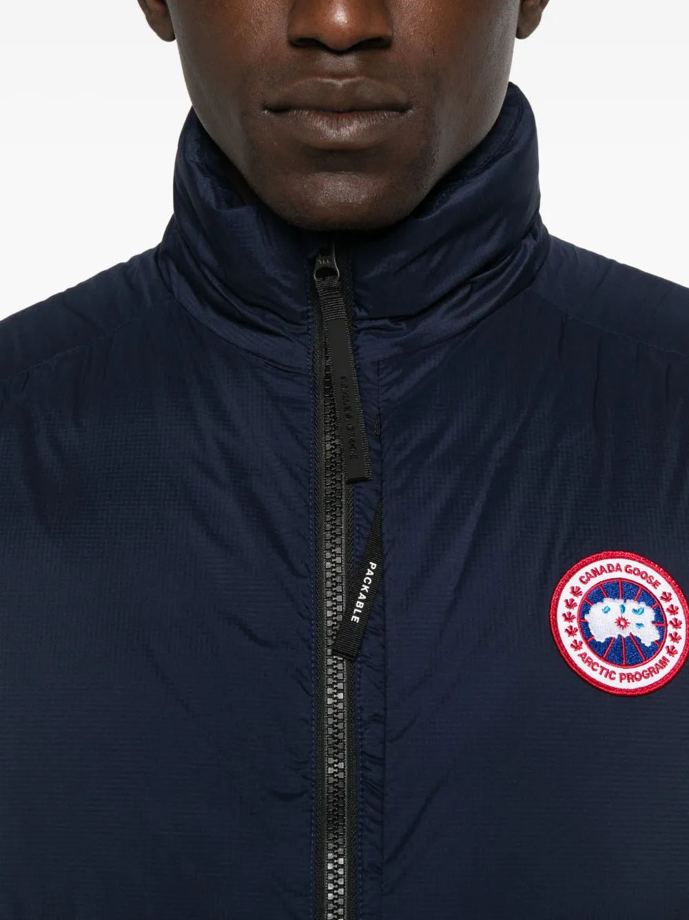 Close-up: navy quilted gilet zip with branded pull and circular logo patch