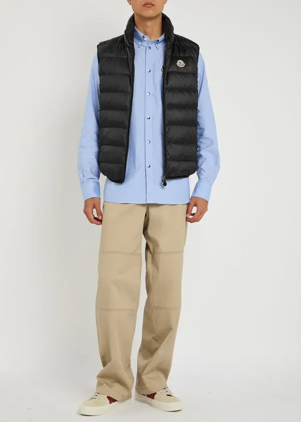 Black Moncler quilted shell gilet worn over a light-blue shirt and beige pants