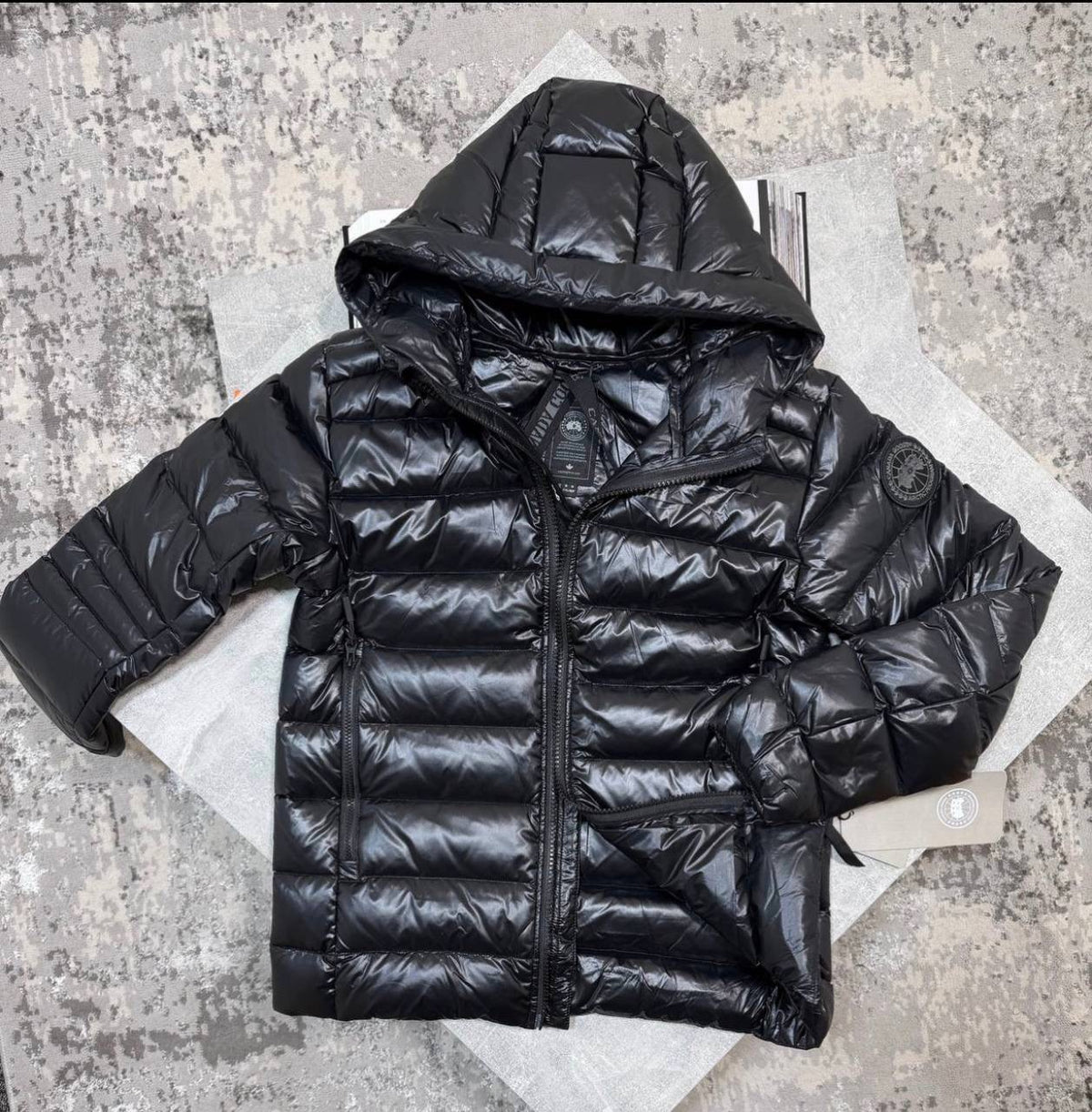 Black hooded puffer jacket with full-zip front, long sleeves, and round sleeve patch