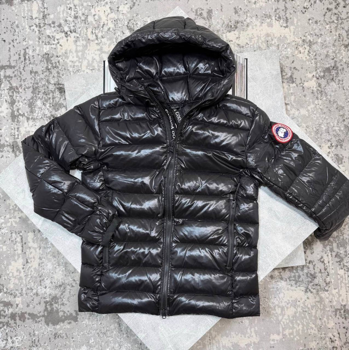 Black hooded puffer jacket with full-zip front and red-bordered round sleeve patch