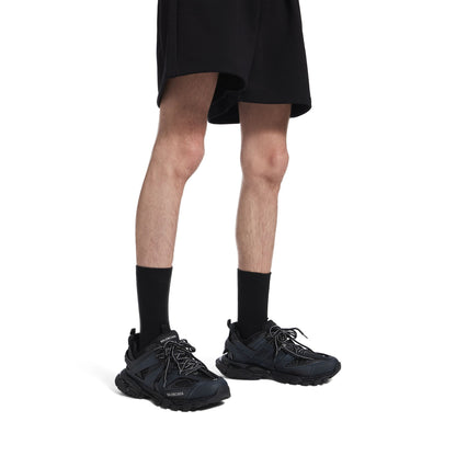 Men's black track sneakers, close leg view with lace-up uppers and thick sole