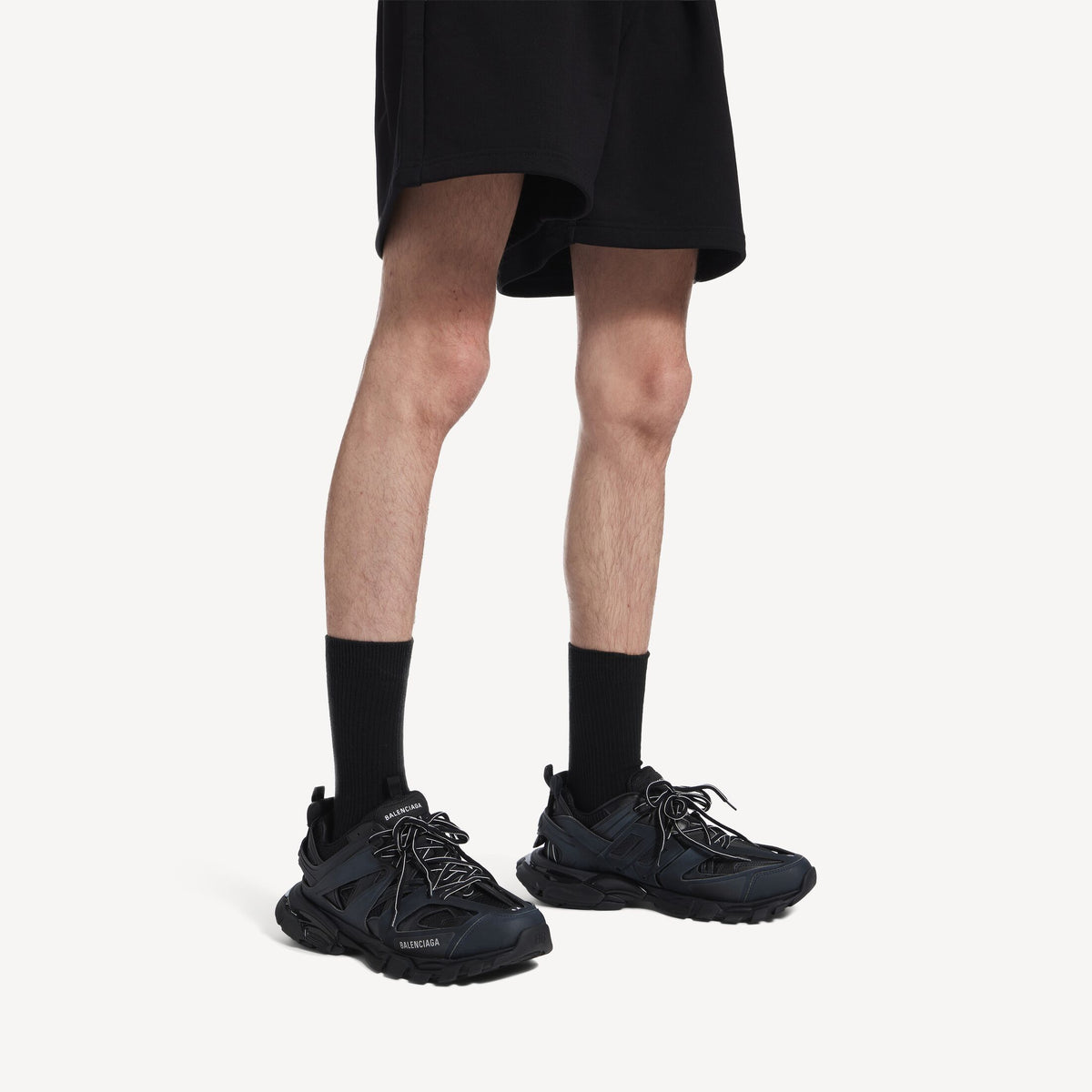 Men's black track sneakers on feet with black socks and chunky tread sole