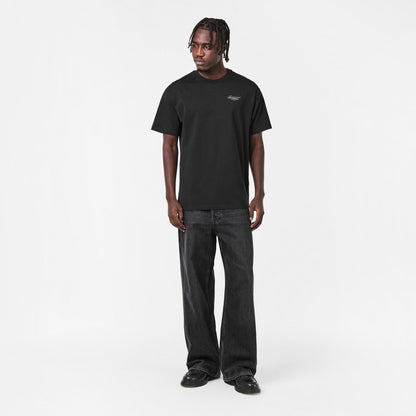 Black crew-neck T‑shirt with small chest logo print, worn with dark jeans