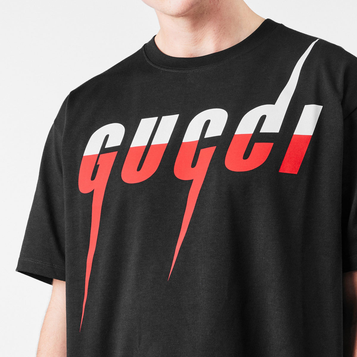 Nahaufnahme: „gucci!“ Schriftprint auf schwarzem T-Shirt, weißer Block mit rotem Strich