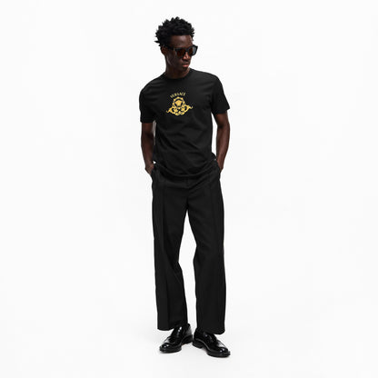 Black T-shirt with gold Medusa crest logo, worn with black trousers