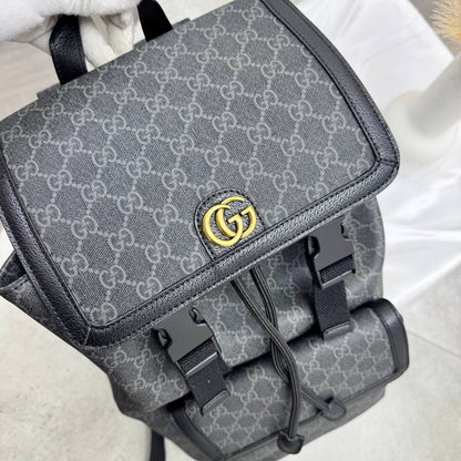 Dark gray GG backpack side panel with gold-tone GG emblem and front buckle details