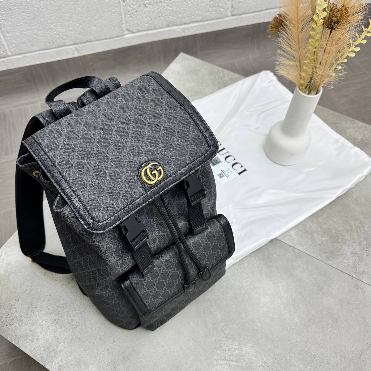 Dark gray GG monogram backpack with front flap, buckle closures, and shoulder straps