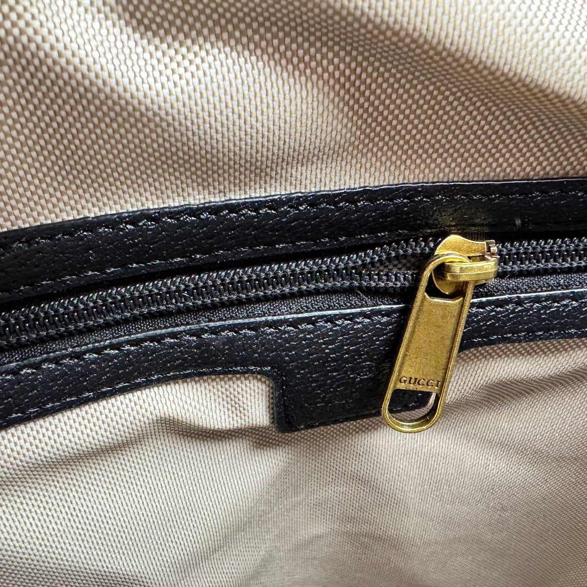 Black zipper pull with gold Gucci GG hardware on dark gray monogram lining