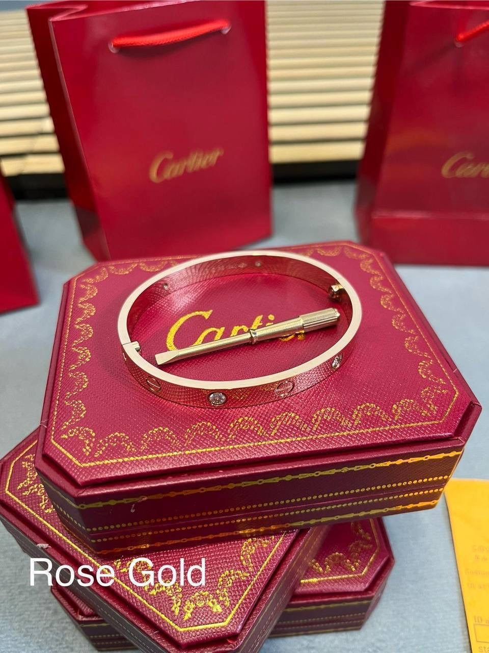 Rose gold love bracelet with small stud detailing on red Cartier gift box