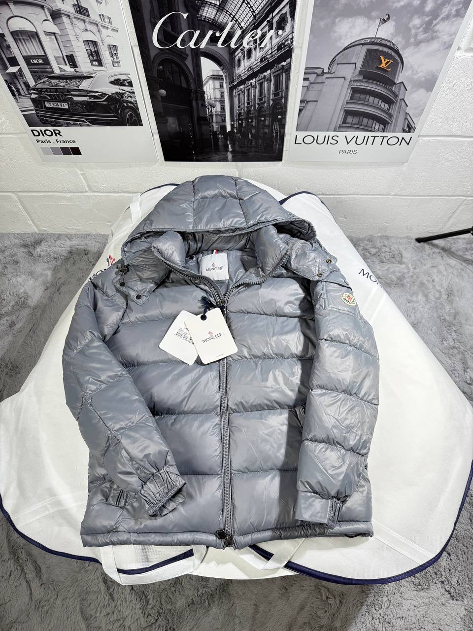 Light gray Moncler puffer jacket with hood and zipper, showing logo patch and tags