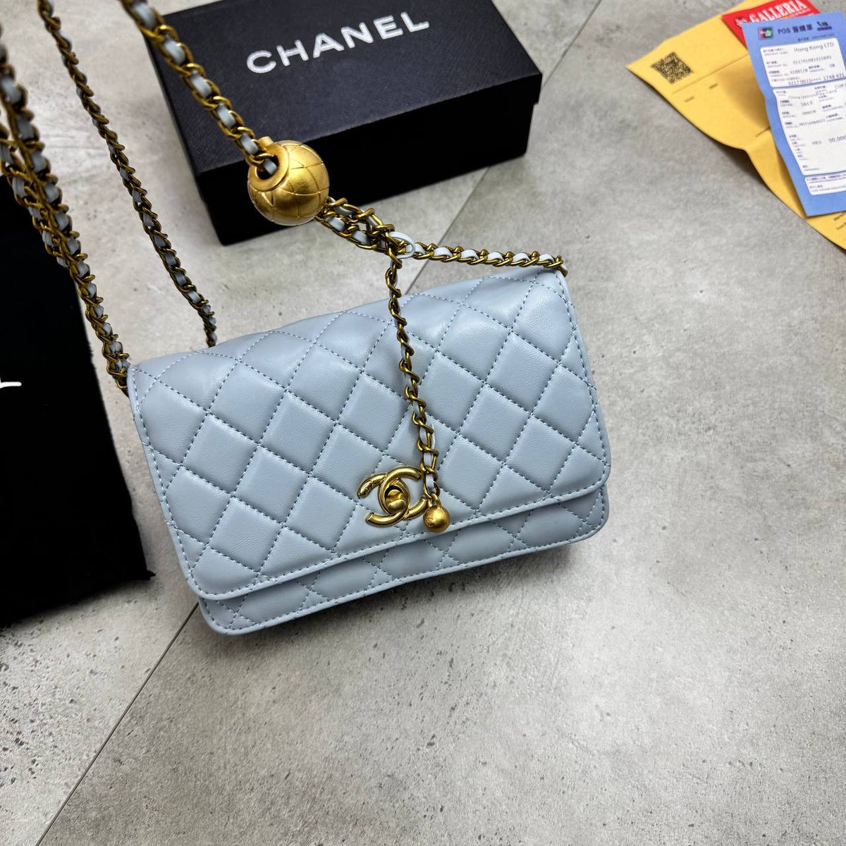 Light blue quilted shoulder bag with gold chain strap and logo charm, flap closed