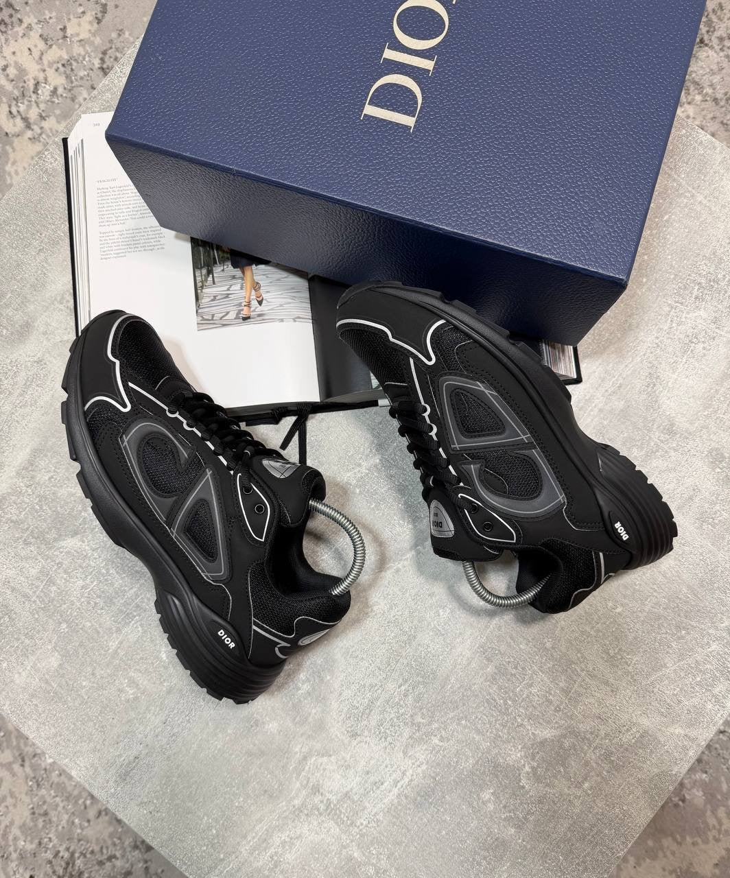 Black lace-up stealth sneakers with textured overlays, gray logo details, and thick tread