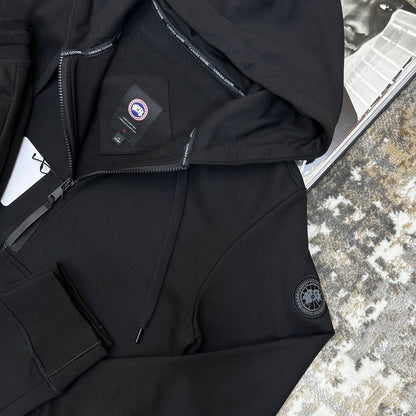 Black tracksuit set close-up with zip-front hooded jacket and logo patch on sleeve