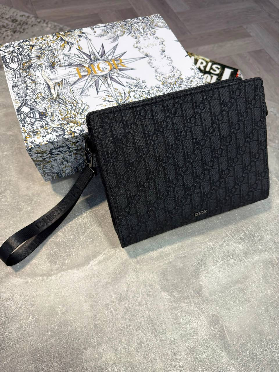 Black monogram pouch with zip top and wrist strap, rectangular silhouette
