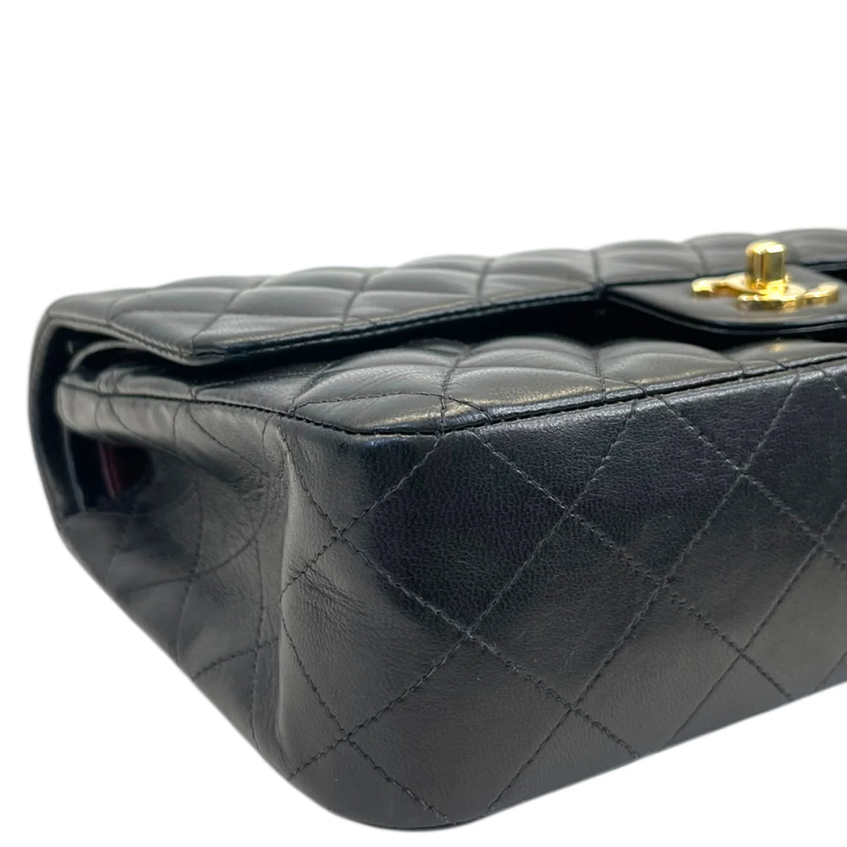Close-up side of dark quilted double flap bag with gold top closure detail