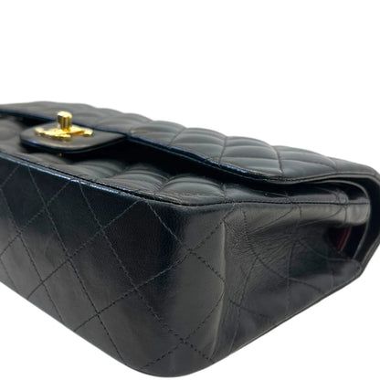 Side view of dark quilted leather double flap handbag with gold clasp hardware