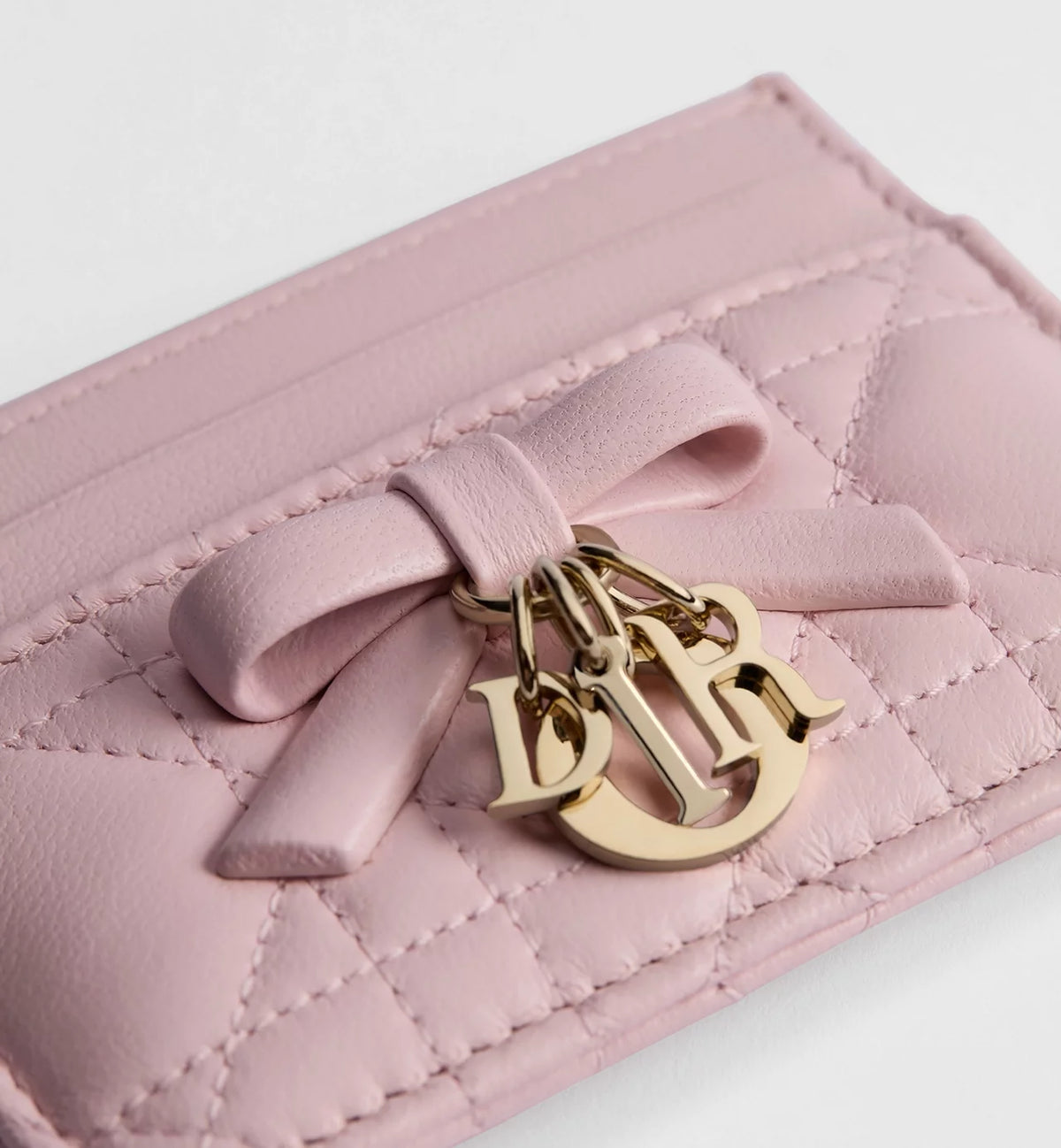 Close-up: pale pink card holder bow and gold-tone key charm on quilted leather
