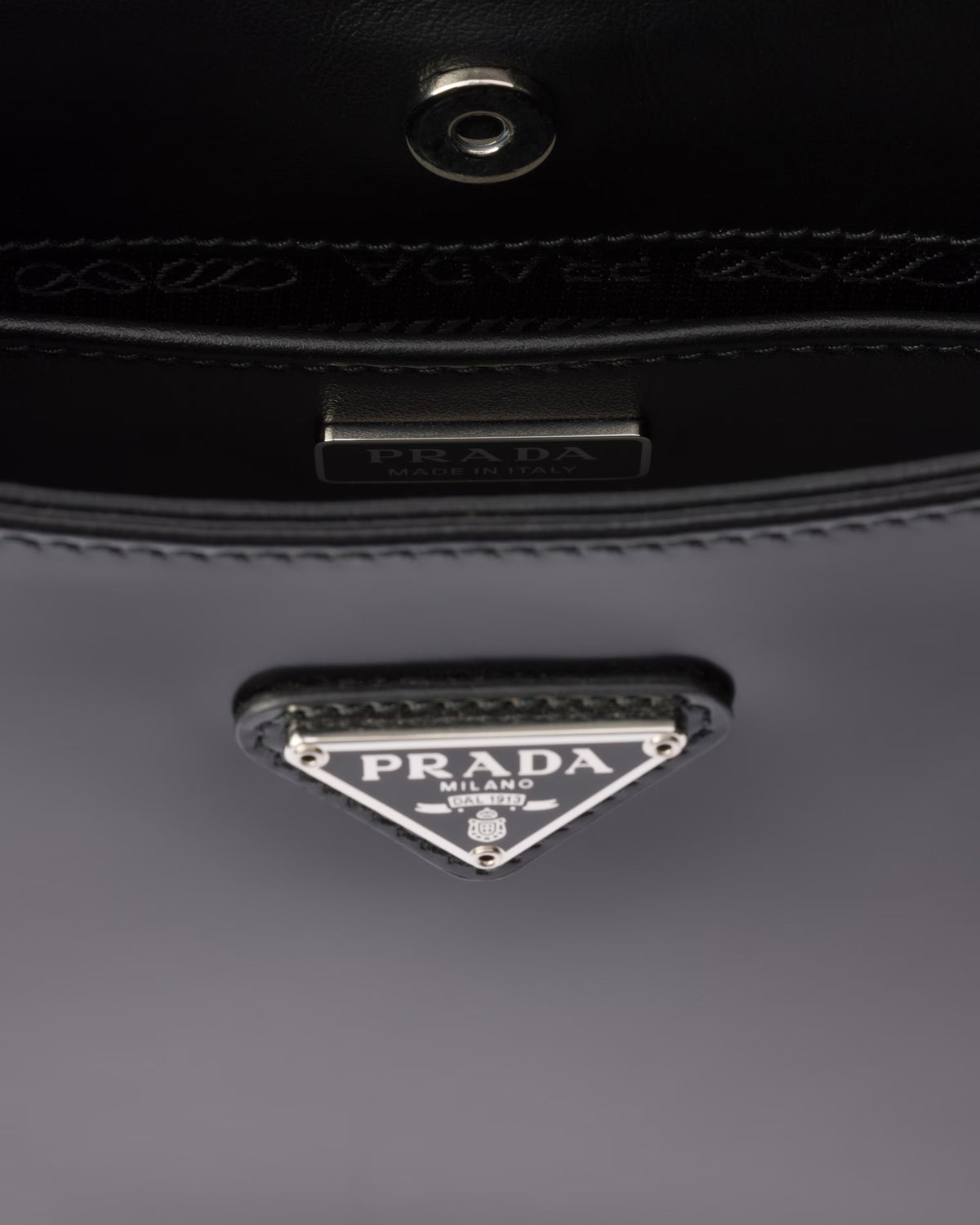 Prada triangle logo on black leather bag, metal clasp and stitching