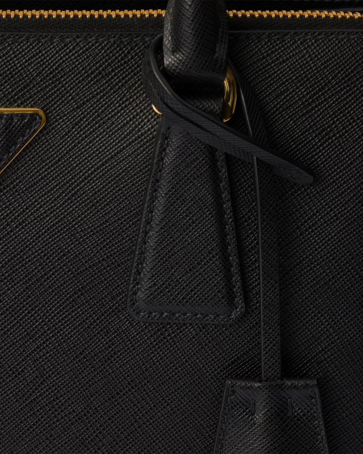 Close-up of black Saffiano bag tassel pulls and gold zipper trim on the front