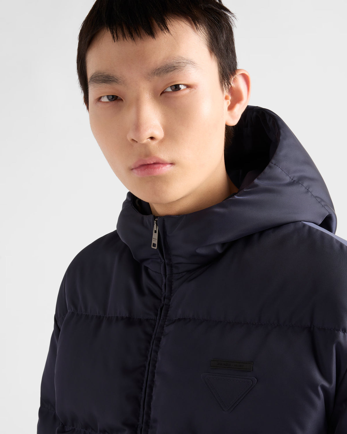 Dark navy hooded puffer jacket with chest logo patch and zip-front at the collar.