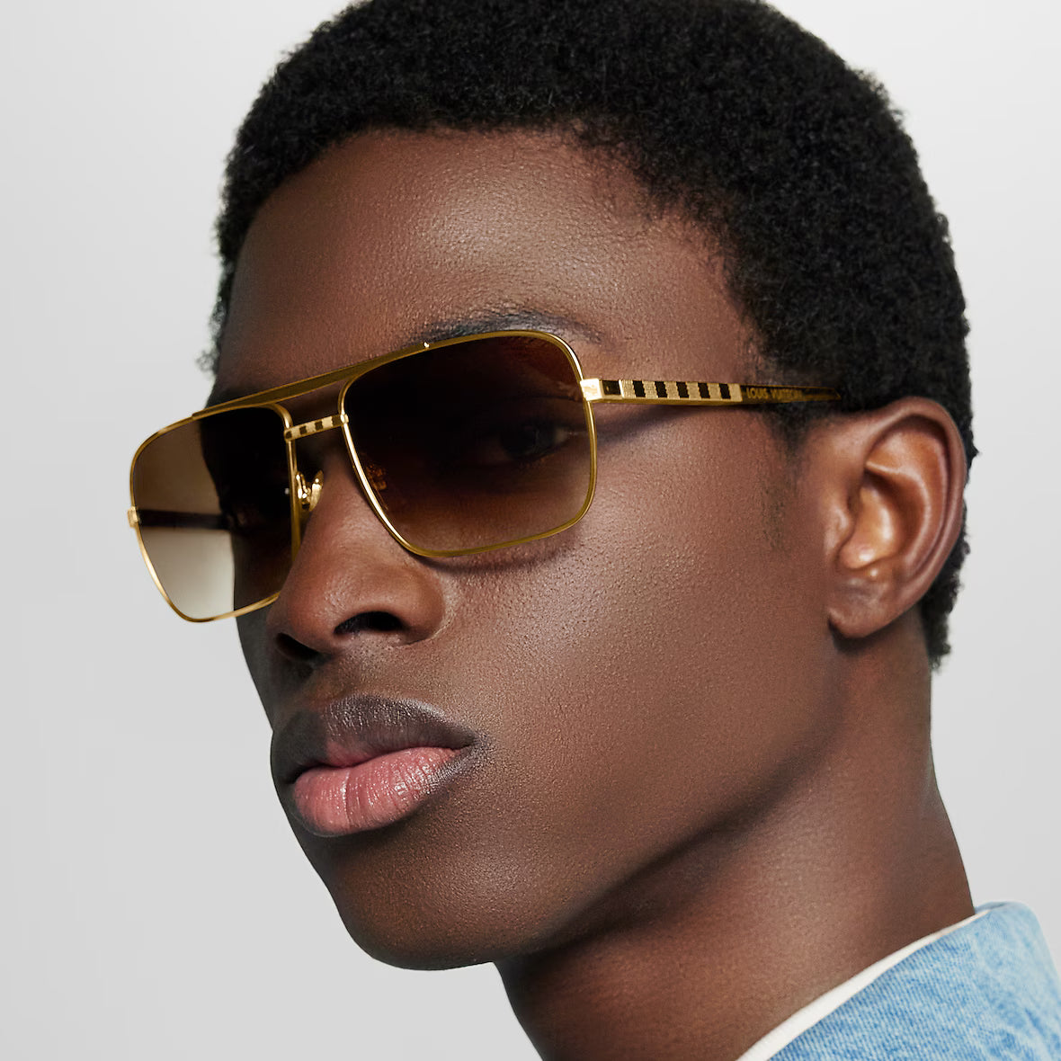 Attitude Sonnenbrille am Modell: eckiger goldfarbener Rahmen, dunkelbraune Gläser