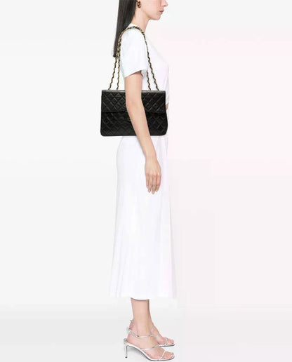 Maxi Classic Flap bag on model’s shoulder; black quilted design with gold chain strap
