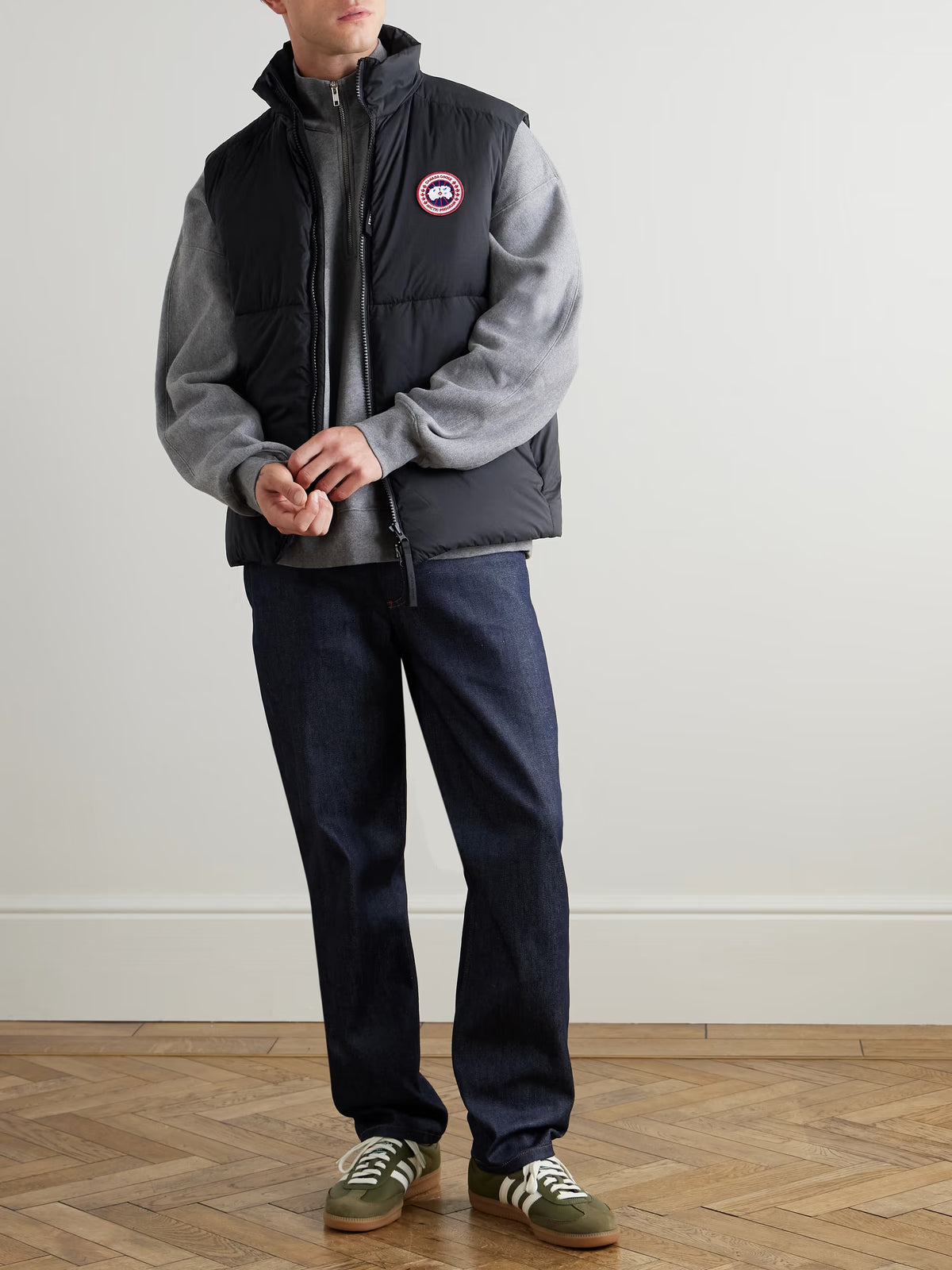 Black down gilet with full-zip front and round chest logo patch, worn over hoodie