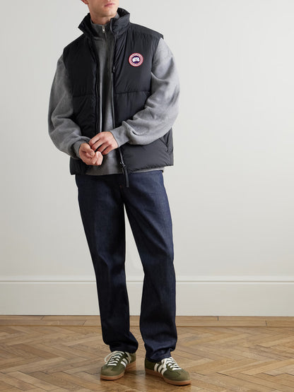 Black down gilet with full-zip front and round chest logo patch, worn over hoodie