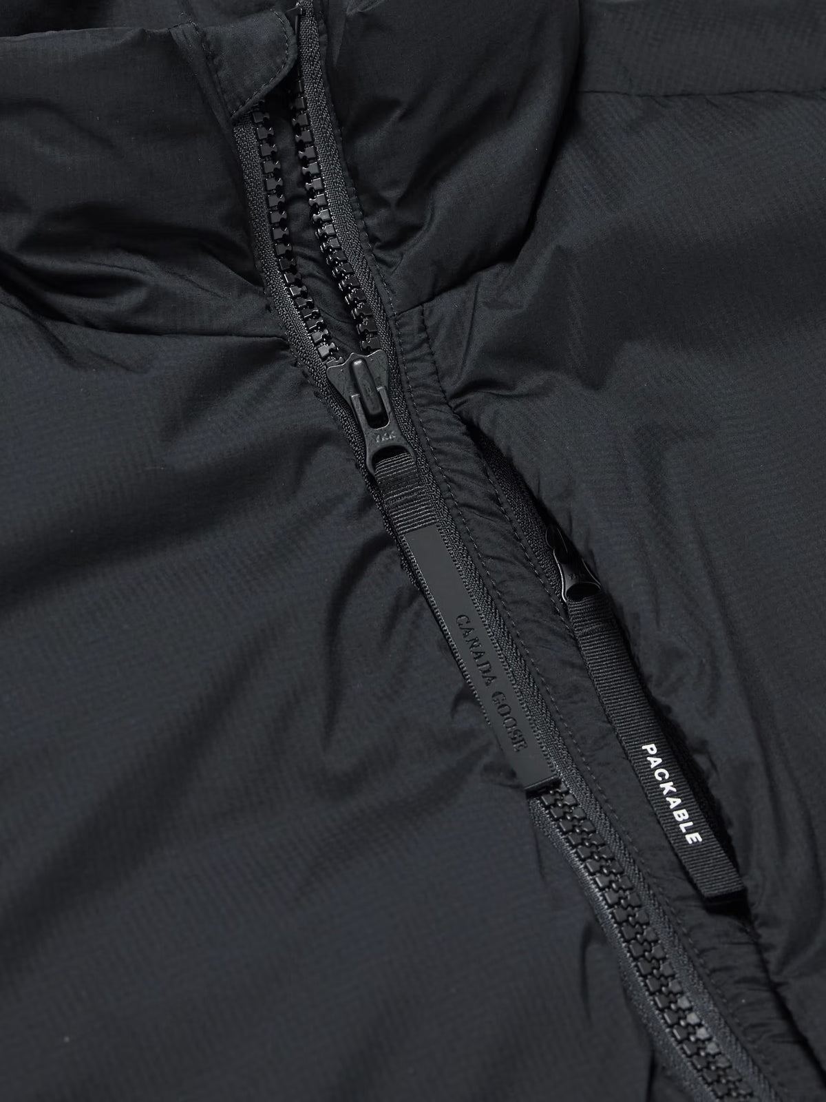 Black ripstop down gilet close-up: full-zip with branded pull tab and pocket opening