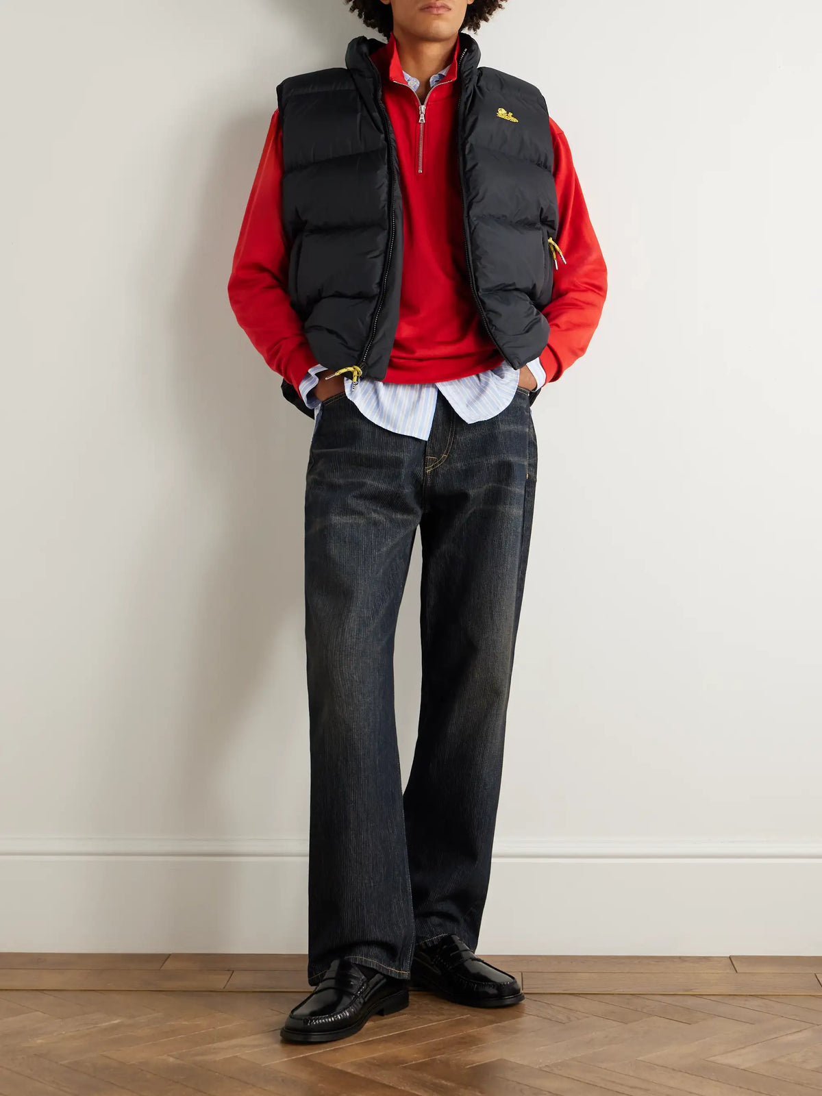 Black quilted logo vest worn over a red hoodie; sleeveless puffer styling