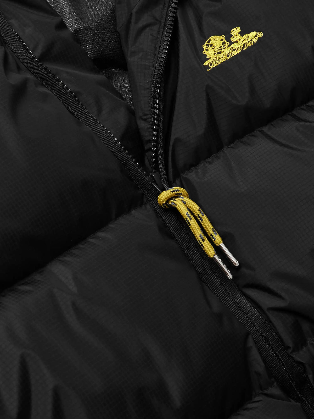 Close-up of black quilted vest zipper with gold drawcord pull and logo detail
